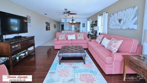 Amplia sala de estar con un televisor de pantalla plana grande, un sofá seccional rosa, un reposapiés de cuero y un mueble de entretenimiento de madera.