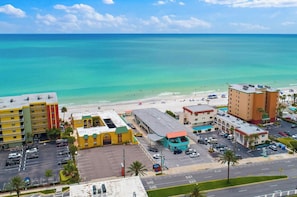 A coastal hotel with multiple buildings, a parking lot, and a beach in the background.