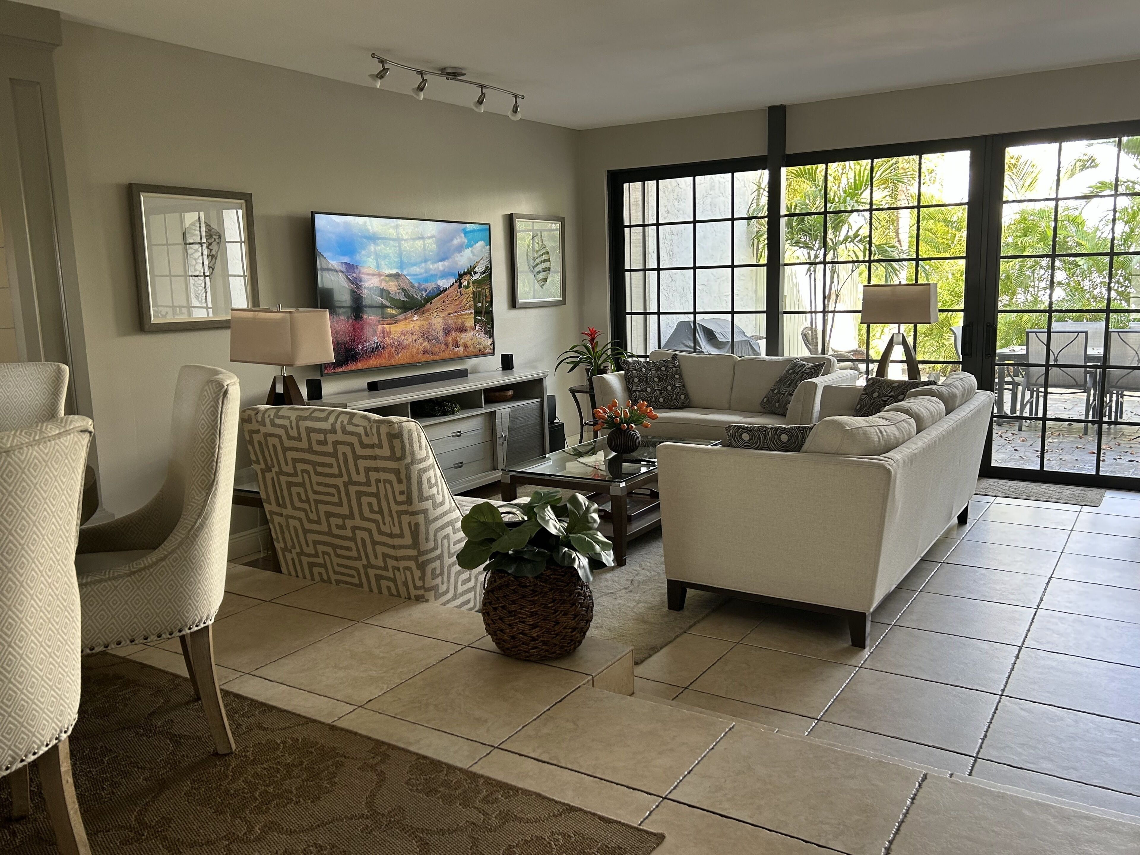 A spacious living room with a large TV, comfortable seating, and a view through large windows.