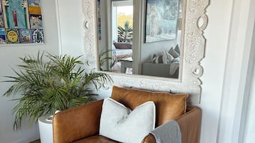 A brown leather sofa with pillows, a striped rug, a potted plant, and a decorative mirror with an ornate frame.