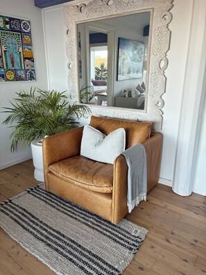 A brown leather sofa with pillows, a striped rug, a potted plant, and a decorative mirror with an ornate frame. - Blue Seas Villa, Sth Avoca Magnificent Beach & Ocean Views  (AVOCA BEACH)