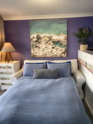 A bedroom with a bed, a nightstand, a lamp, a potted plant, and a beach-themed wall hanging. - Blue Seas Villa, Sth Avoca Magnificent Beach & Ocean Views  (AVOCA BEACH)