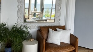 Ein Zimmer mit einem braunen Ledersofa, einem weißen Beistelltisch und einem großen Spiegel mit dekorativem Rahmen.