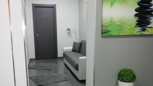 Un interior moderno con un sofá gris, una lámpara de mesa pequeña, una planta en maceta y un cuadro con una pila de piedras.