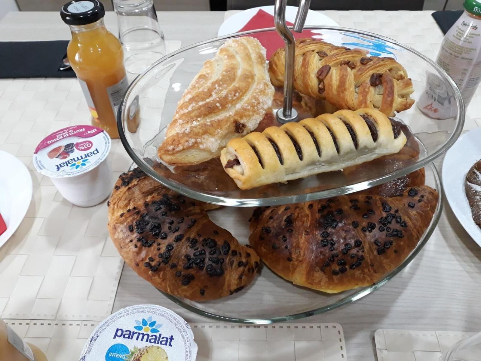 Un présentoir en verre contenant des pâtisseries et une bouteille de jus d’orange, le tout posé sur une table.