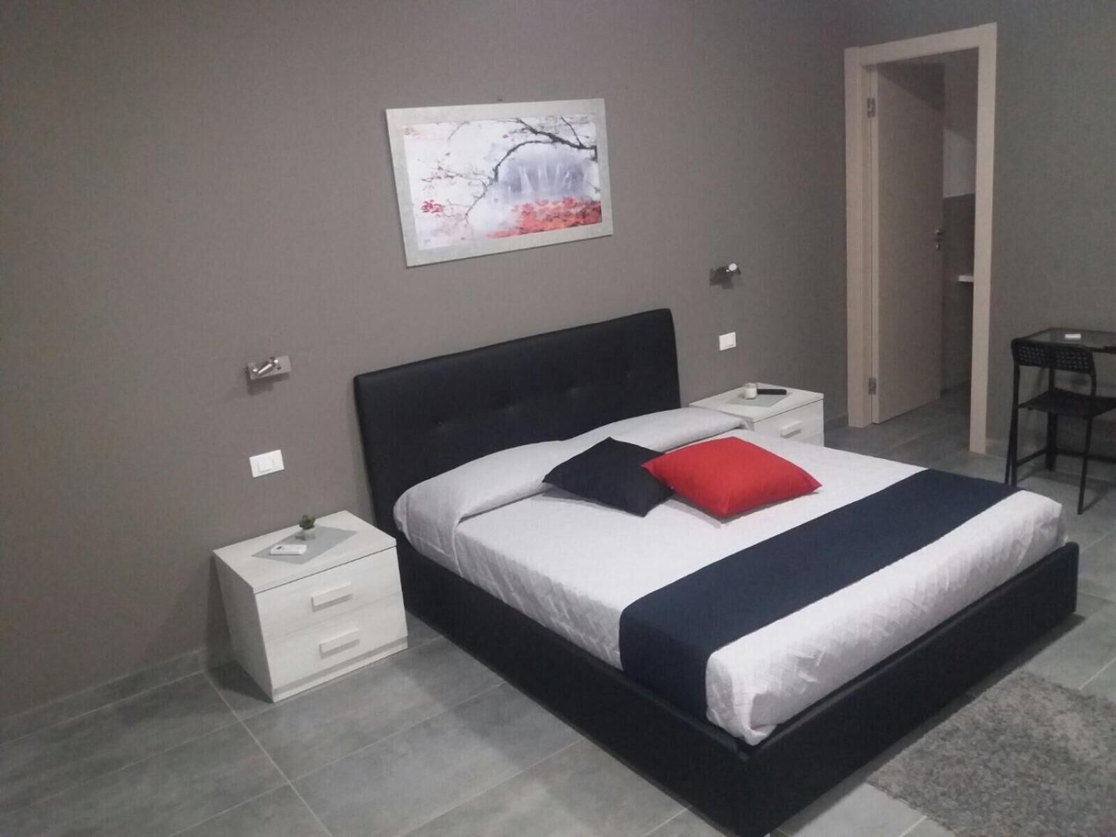 Une chambre à coucher moderne avec un lit, des tables de chevet, une chaise et un tableau accroché au mur.
