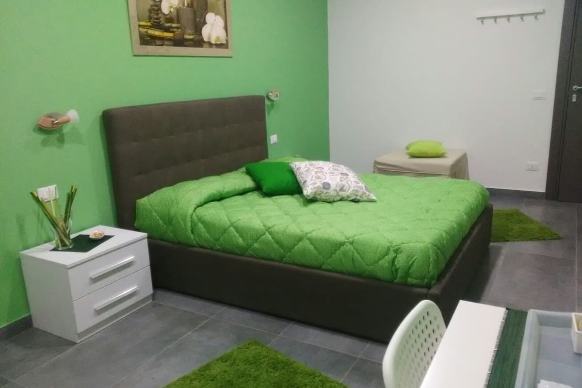 A bedroom with a green bedspread, a bedside table with a lamp, and a small nightstand with a lamp.