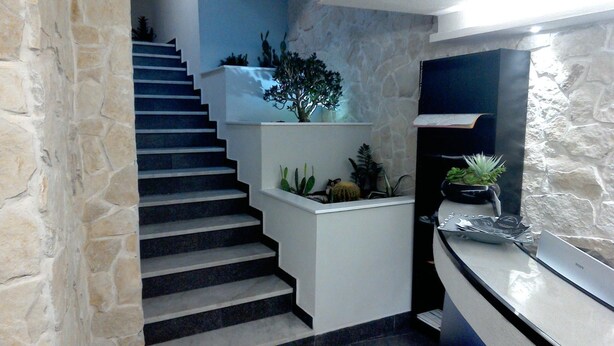 Una escalera moderna con un lateral de pared de piedra y otro de pared blanca, que conduce a un rellano con una pequeña exhibición de plantas.