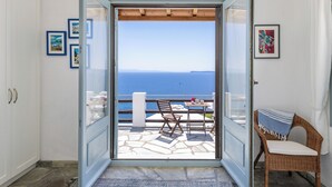 A room with a view of the sea, a wicker chair, a table, and a door leading to an outdoor area with a table and chairs. - Villa Kalyves Armenopetra - Beautiful  Pool - Amazing Sea Views -Walk to Beaches (Neo Klima)