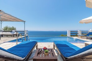 A poolside area with lounge chairs, a table with a plant, and a view of the sea.