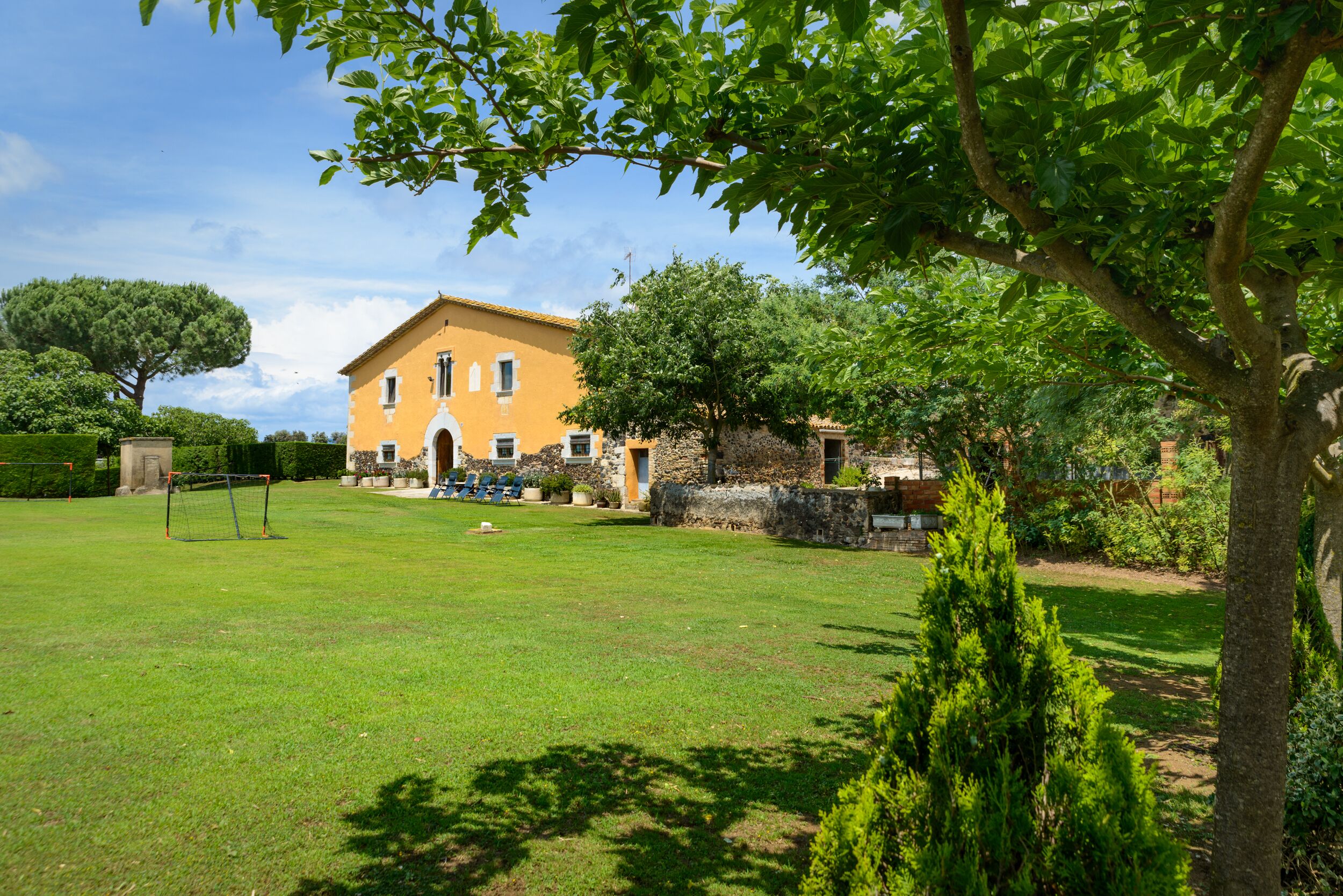 A spacious lawn with a stone wall and a yellow building with arched windows.