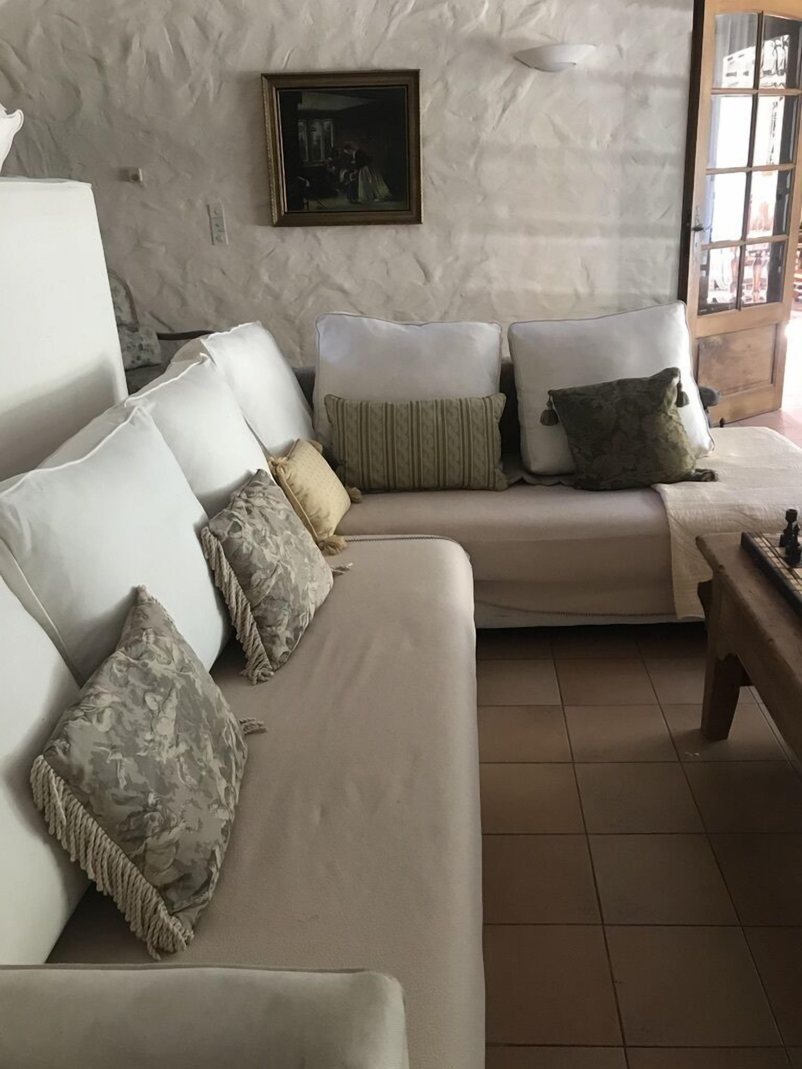 A living room with a beige sofa, patterned cushions, a wooden coffee table, and a framed painting on the wall.