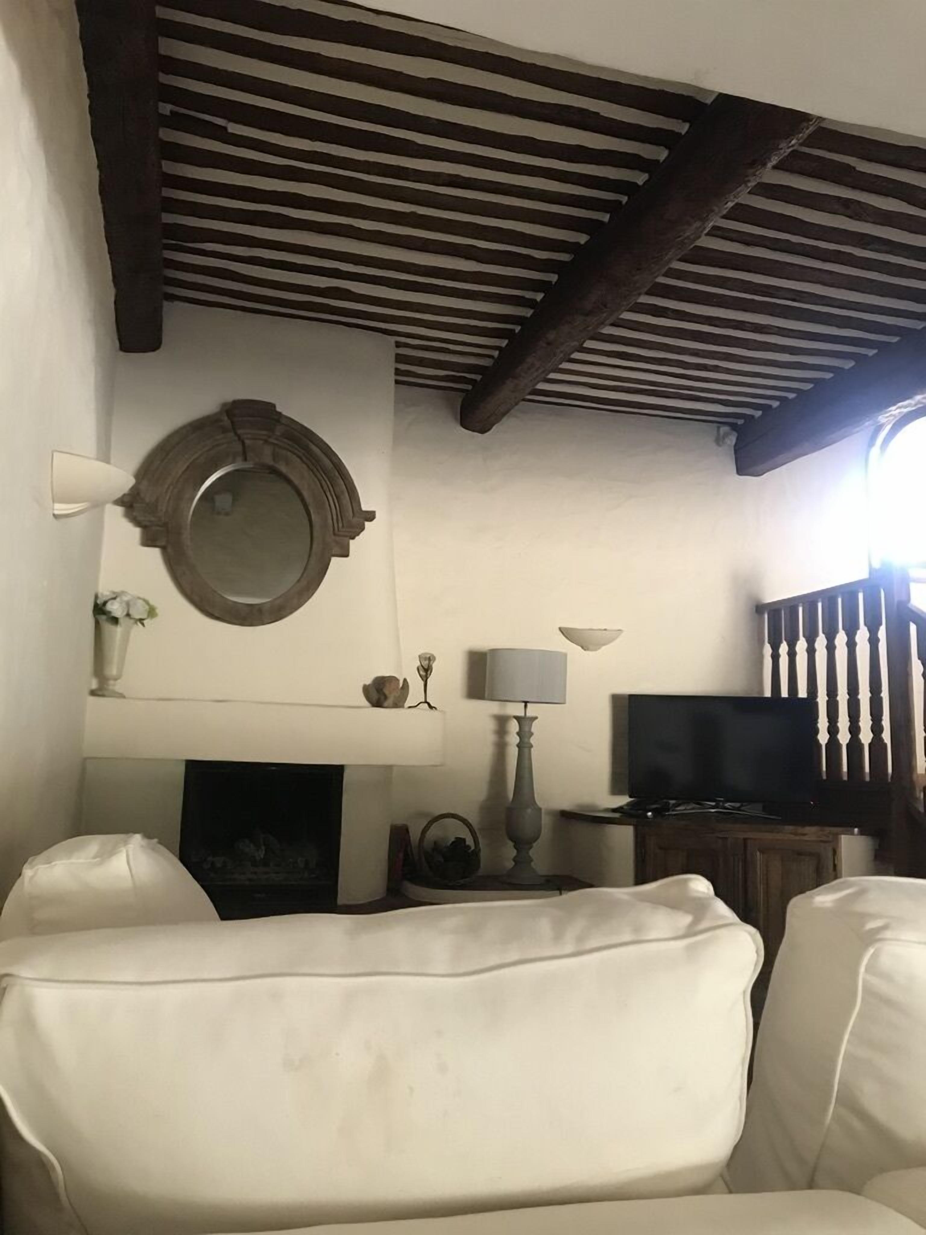 A living room with a white sofa, a fireplace, a television, and a ceiling with exposed beams.