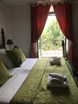 Un lit bien fait, avec une literie verte et blanche, une lampe de chevet et une fenêtre ornée de rideaux rouges.