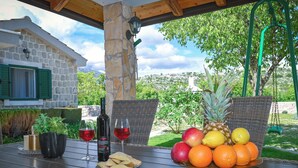 A table with a bottle of wine, glasses, a plate of crackers, and a fruit basket.