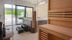 A modern spa area with a hot tub, wooden seating, and a glass door leading to a scenic outdoor view.