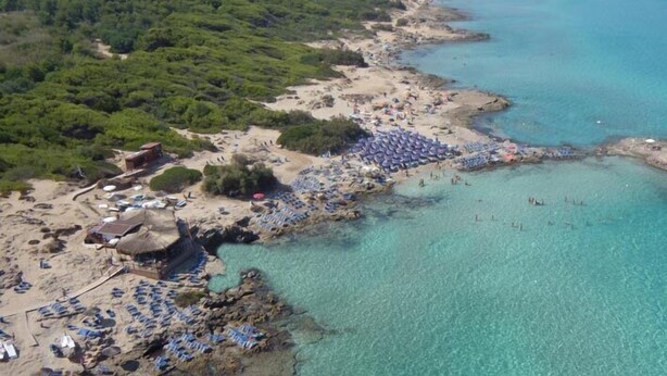 An aerial view of a beach with clear turquoise waters, a sandy shore, and several beach umbrellas. - Villa CARLOTTA Magnificent Ancient CASEDDHU by the sea (Racale Torresuda)