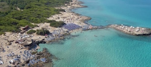 Vista aérea de una playa con aguas turquesas cristalinas, una orilla arenosa y varias sombrillas.
