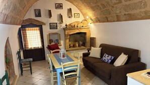 A cozy living room with a stone fireplace, a dining table, and a sofa. - Villa CARLOTTA Magnificent Ancient CASEDDHU by the sea (Racale Torresuda)