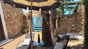 A patio with two lounge chairs, a small table, and a striped umbrella. - Villa CARLOTTA Magnificent Ancient CASEDDHU by the sea (Racale Torresuda)