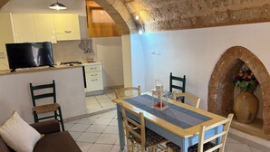 A cozy living area with a sofa, a dining table with chairs, a kitchen with a TV, and a stone archway. - Villa CARLOTTA Magnificent Ancient CASEDDHU by the sea (Racale Torresuda)