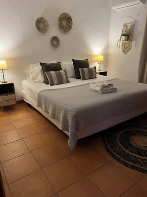 Una cama bien hecha con una colcha estampada, dos lámparas de noche y decoración en la pared.
