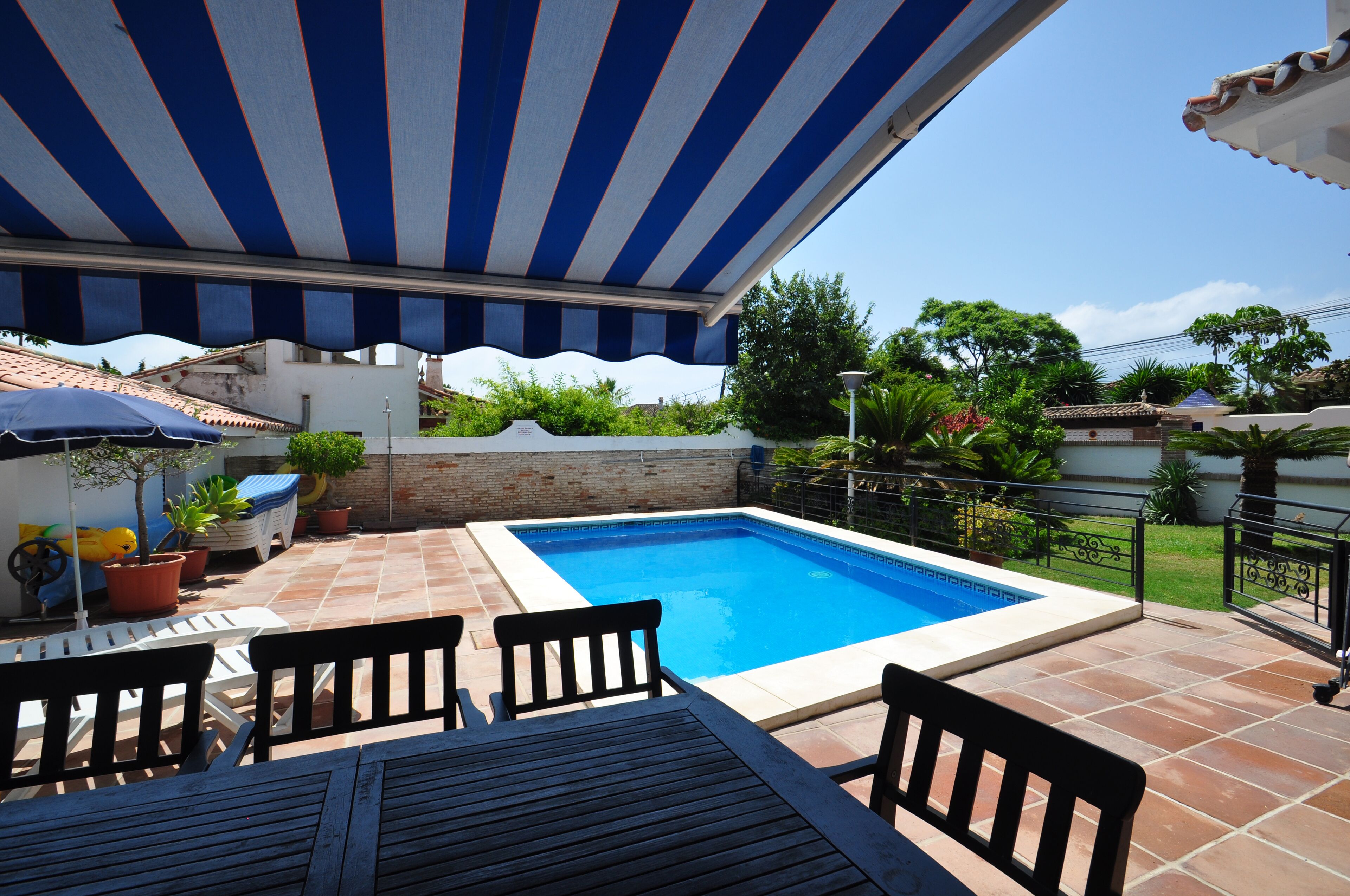 A swimming pool with a tiled deck, surrounded by potted plants and outdoor furniture.