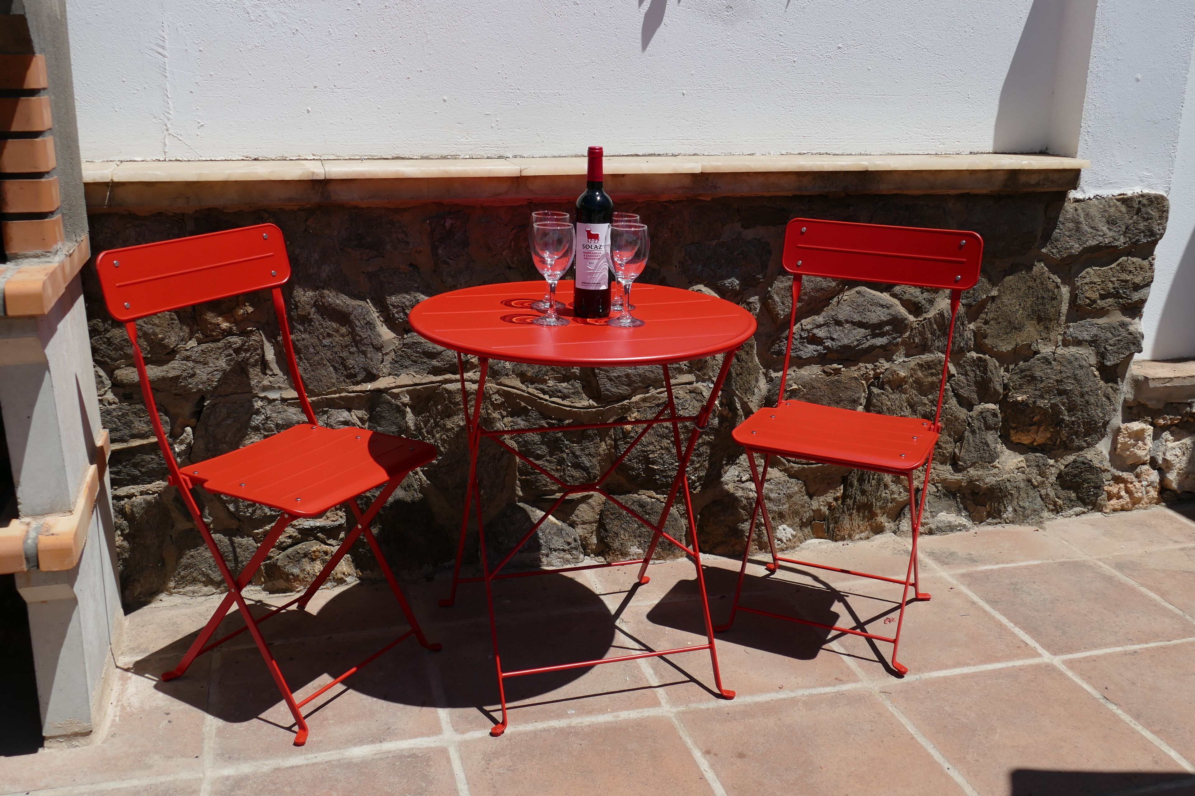 Ein roter Metalltisch mit zwei Stühlen und einer Weinflasche darauf.