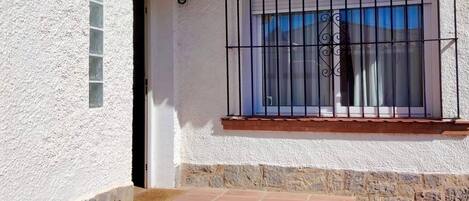 A white building with a balcony, a window with metal bars, and a potted plant.