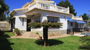 Un bâtiment blanc doté d’un balcon, d’un mur en pierre et d’un palmier dans le jardin.