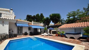 Une piscine dotée d’une terrasse carrelée, de chaises longues et d’un patio couvert agrémenté de parasols.