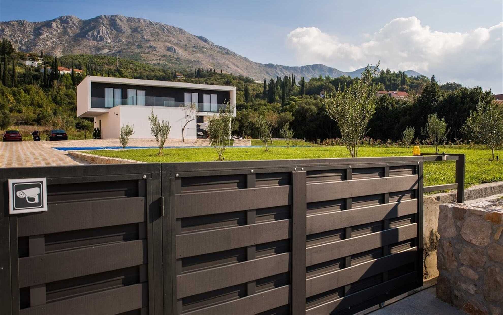A modern building with a flat roof and large windows, surrounded by greenery and mountains.