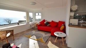Un salon moderne avec un canapé rouge, une petite table ronde et une vue sur la mer grâce à de grandes fenêtres.