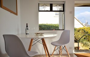 Een eetgedeelte met een ronde tafel, twee stoelen, een fles en een schaal fruit.