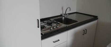 A kitchen with white cabinets, a black countertop, a stainless steel sink, and a gas stove.