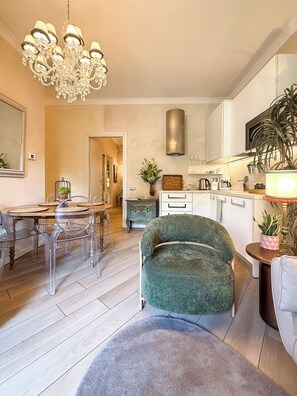 A modern kitchen with a chandelier, a dining area with a table and chairs, and a green armchair.
