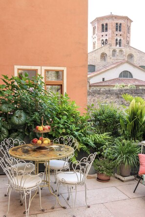 A round table with chairs, a potted plant, and a building with a tower in the background.