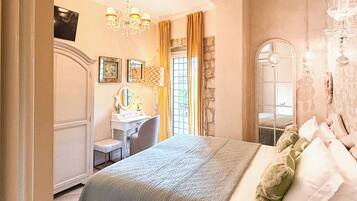 A bedroom with a bed, a desk, a chair, a mirror, and a chandelier.
