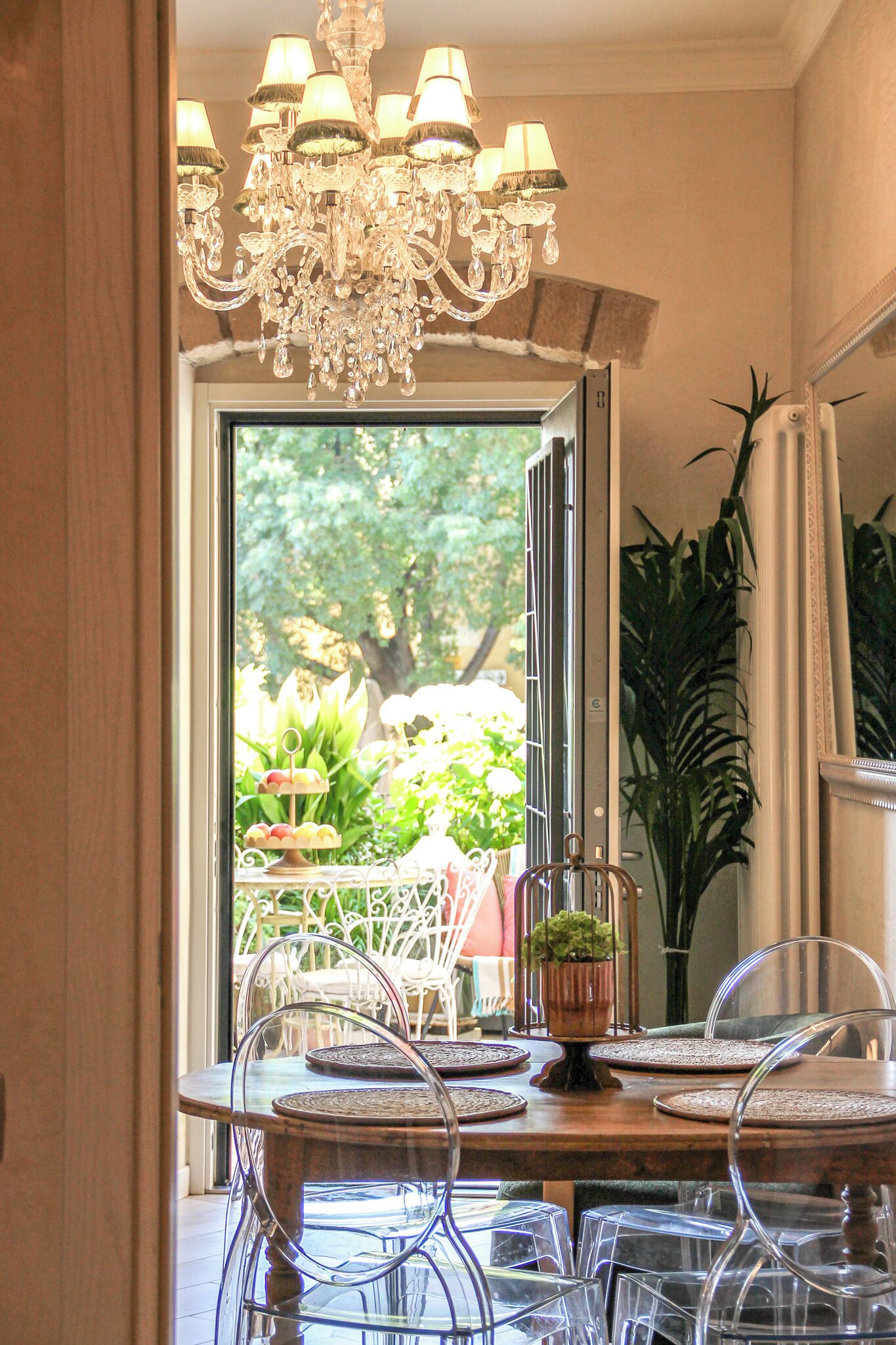 Comedor con candelabro, una mesa con sillas y vista a la vegetación exterior.