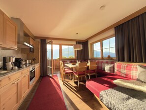 A cozy kitchen with wooden cabinets, a dining area with a red sofa and table, and large windows offering a mountain view.