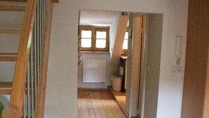 Eine Holztreppe führt zu einem Schlafzimmer mit Dachschräge und Blick auf einen Küchenbereich.
