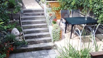 Eine Garten-Terrasse mit Tisch und Stühlen, umgeben von Pflanzen und einer Steintreppe.