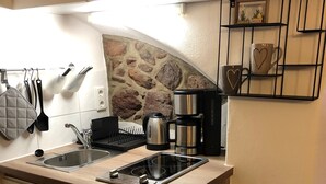 A compact kitchen with a stone backsplash, a coffee maker, and a small dining area with a table and chairs. - modern equipment in historic walls (Görlitz)