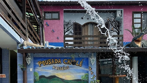 En swimmingpool med et skilt, der viser "Pousada Chêle Pássios", og et muralmaleri af et landskab.