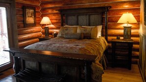 A log cabin-style bedroom with a large bed, two bedside tables with lamps, and a framed picture on the wall. - Ranches at Belt Creek (Belt)