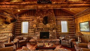 A log cabin interior with a stone fireplace, leather furniture, and mounted animal heads. - Ranches at Belt Creek (Belt)