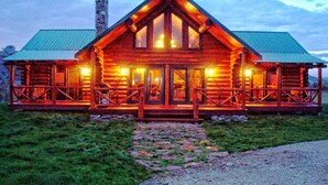 A log cabin with a central entrance, a porch with railings, and a stone pathway leading to the door. - Ranches at Belt Creek (Belt)