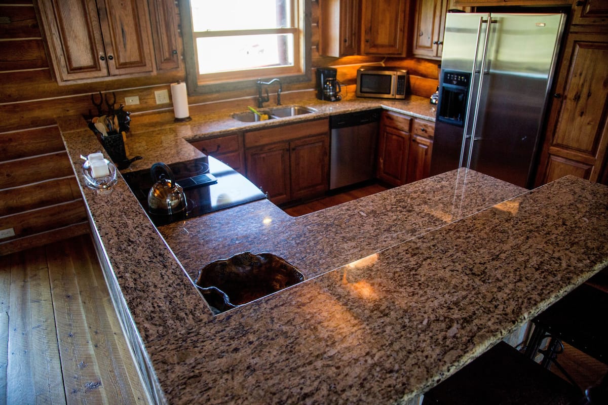 A kitchen with granite countertops, wooden cabinets, stainless steel appliances, and a window providing natural light.