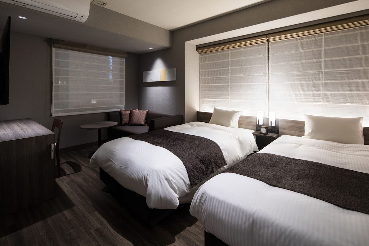 A hotel room with two beds, a small table, a sofa, and a TV.