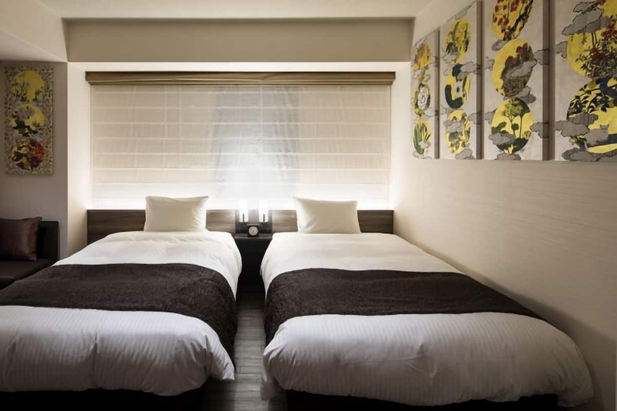 A twin room with two beds, a sofa, a small table, and a window with blinds.